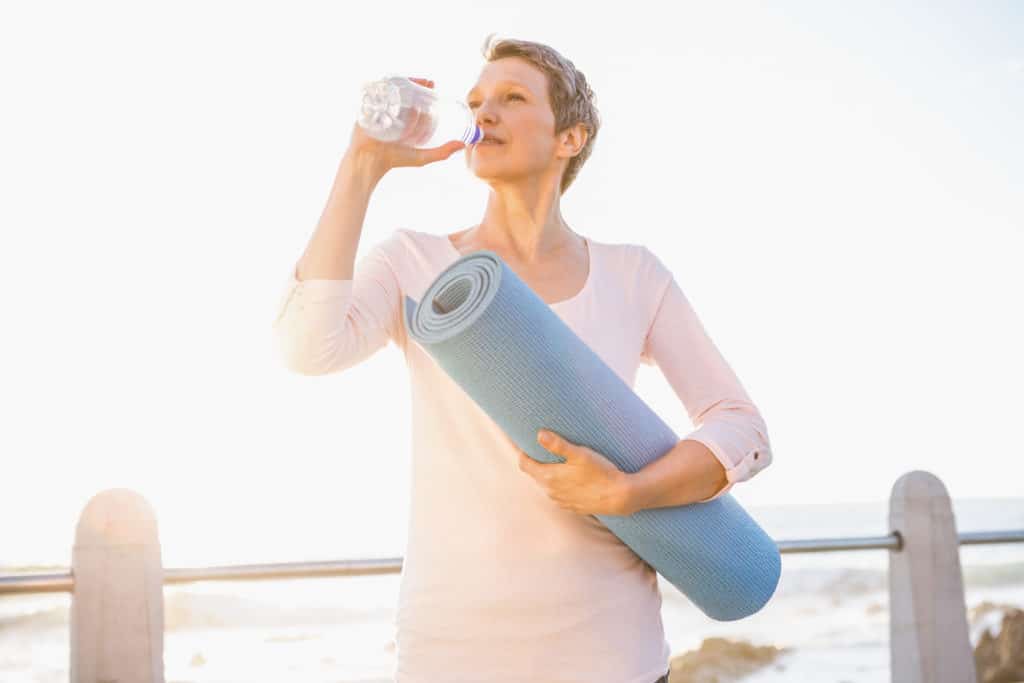 woman holding exercise mat and drinking from water bottle